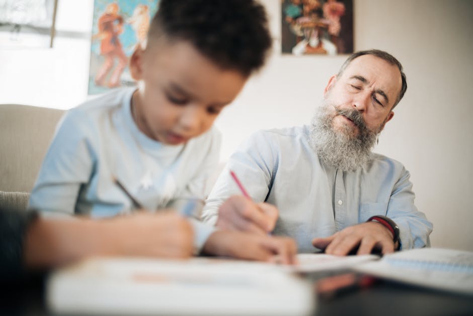 A bearded grandfather helps his grandson with writing indoors.