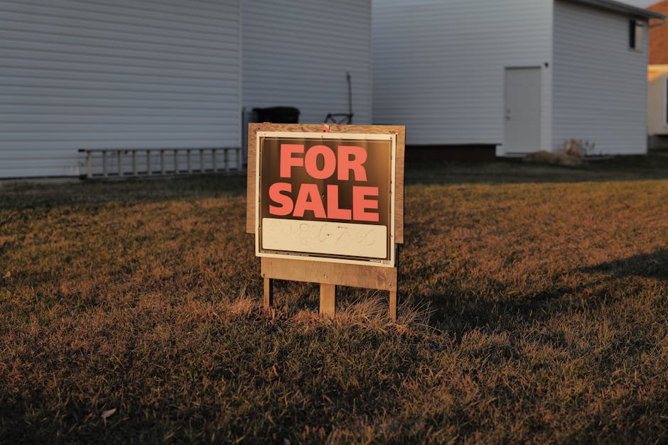 Close-up of a 'For Sale' sign in a suburban yard, indicating a property for sale.