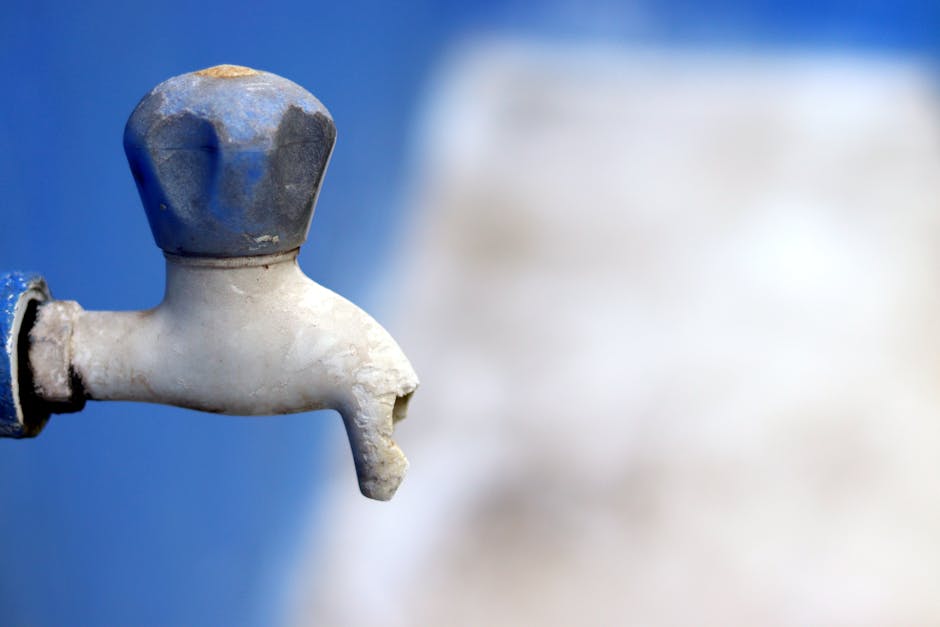 Detailed image of a broken faucet against a blurred blue background, emphasizing neglect.